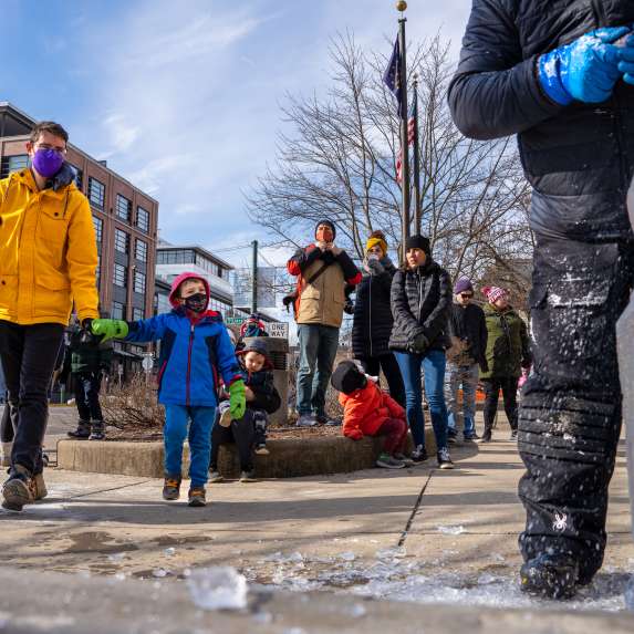 A dad holding his small son's hand as they approach a live carving demonstration during Freezefest