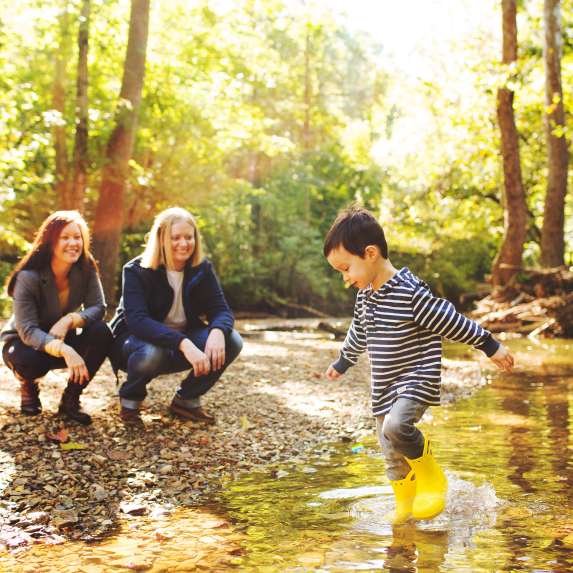 A lesbian couple watching their son play in a creek