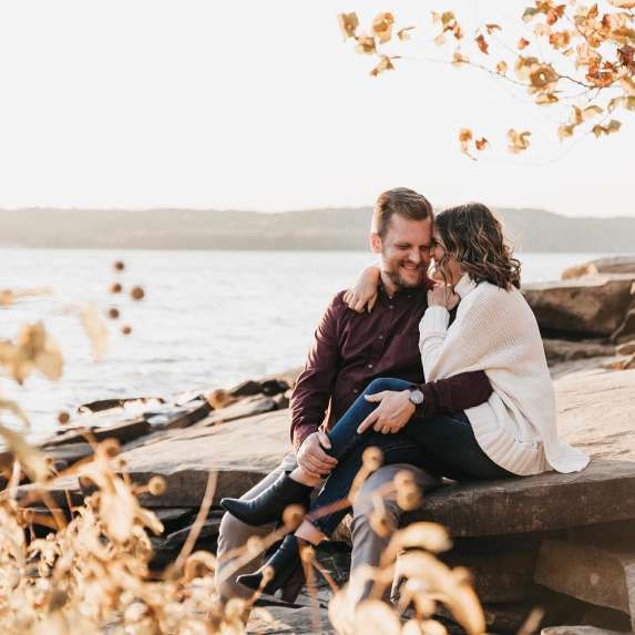 A couple sitting on the rocky shore of Monroe Lake during fall