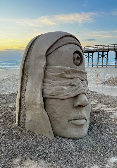 Sand sculpture of a large head with a blindfold on. In the middle of the forehead is a large eye.