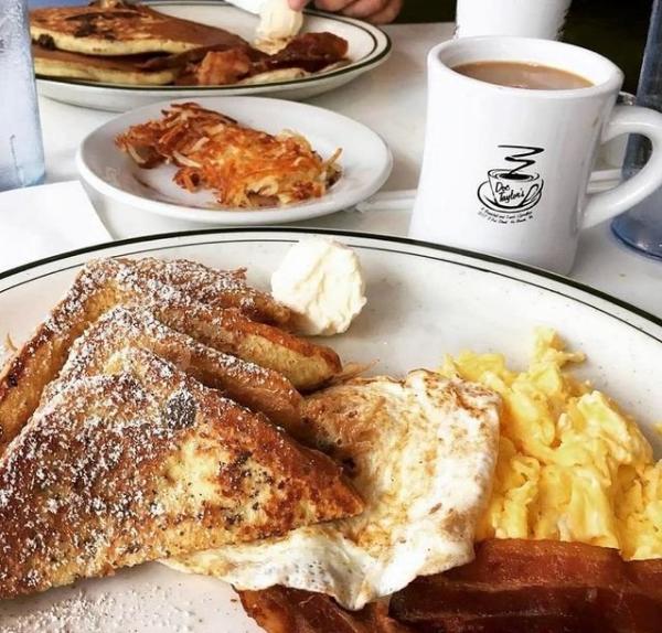 A breakfast of french toast, eggs, bacon, hash browns, and coffee.  