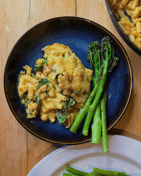 A plate of mac and cheese and tenderstem broccoli on a dark blue plate