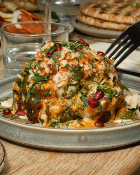 A plate of cauliflower with cheeses, sauce, pomegranate seeds piled on a plate
