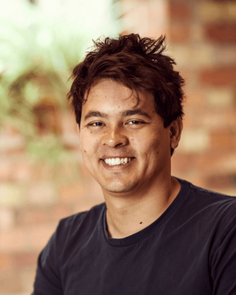 An image of a man smiling brightly and showing his teeth, his hair is black and he is wearing a navy top.