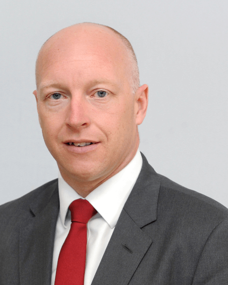 A man looking at the camera and wearing a red tie with a grey blazer and white shirt.