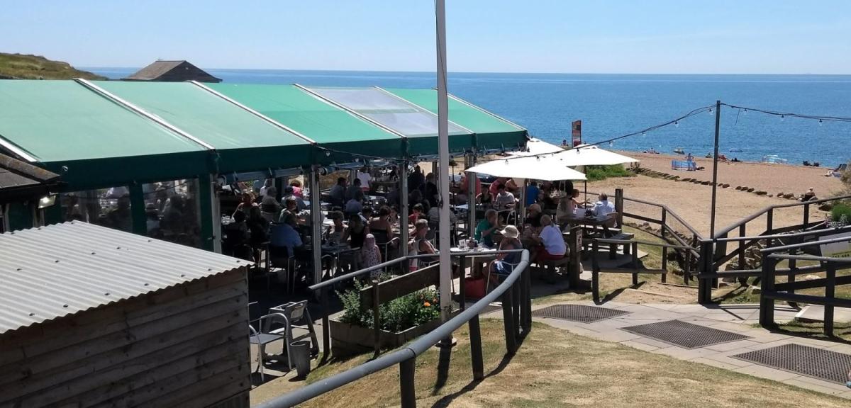 Outside the Hive Beach Cafe at Burton Bradstock in Dorset, with the beach in the background