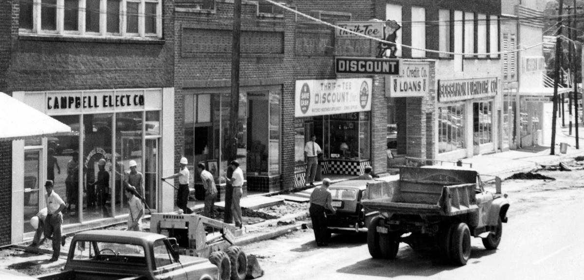 Workers in hard hats building new sidewalks in 1971 outside Campbell Electric Co., Thrif-Tee Discount, Home Credit and Sossamon Furniture in Sylva, NC