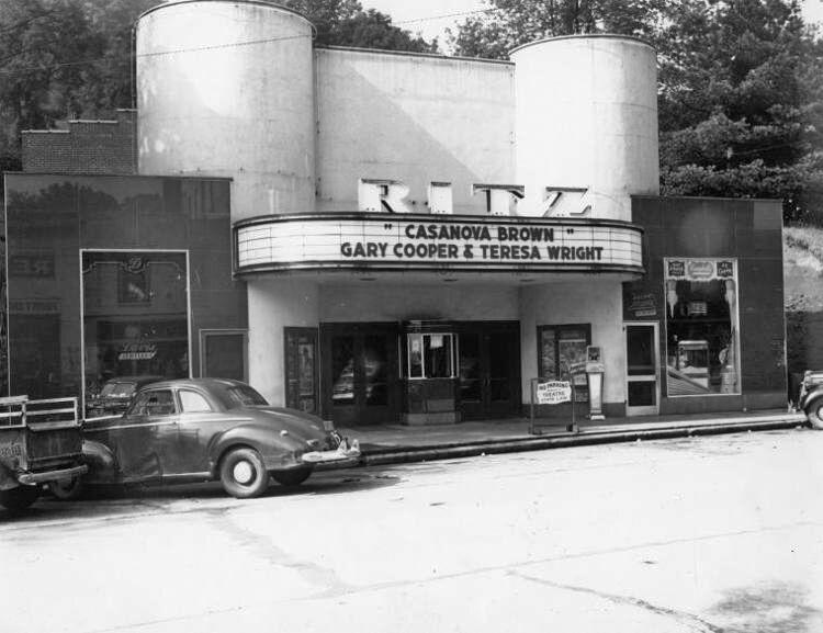 A black-and-white photograph of the historic Ritz movie theater, featuring an Art Deco facade with two large, cylindrical towers on either side of the entrance. The marquee advertises the film "Casanova Brown" starring Gary Cooper and Teresa Wright. Vintage 1940s-era cars are parked along the street in front of the theater.