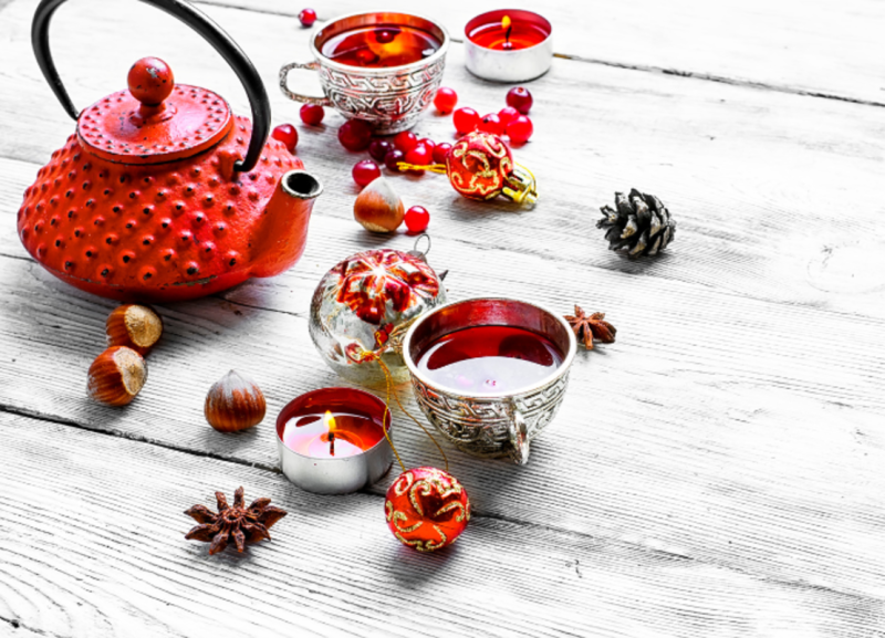 Image is of a tea pot, cup of tea, candles and ornaments next to it.