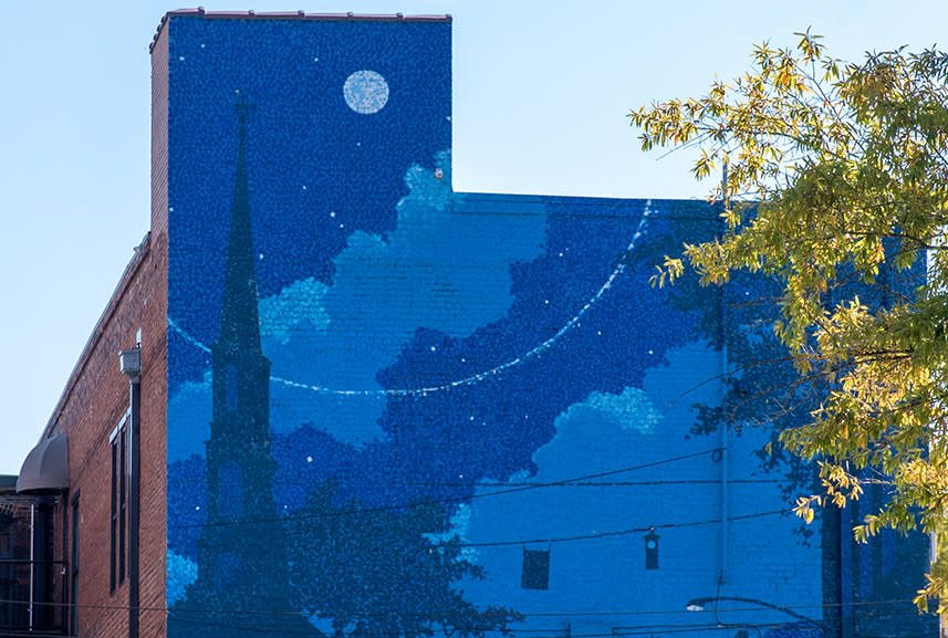 Mural on building that is painted in several colors of blue with images of a church and buildings on Franklin St., Chapel Hill