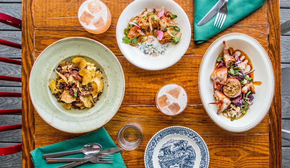 Overhead view of table with two entrees with cocktails and side dish at Odd Duck in Austin Texas