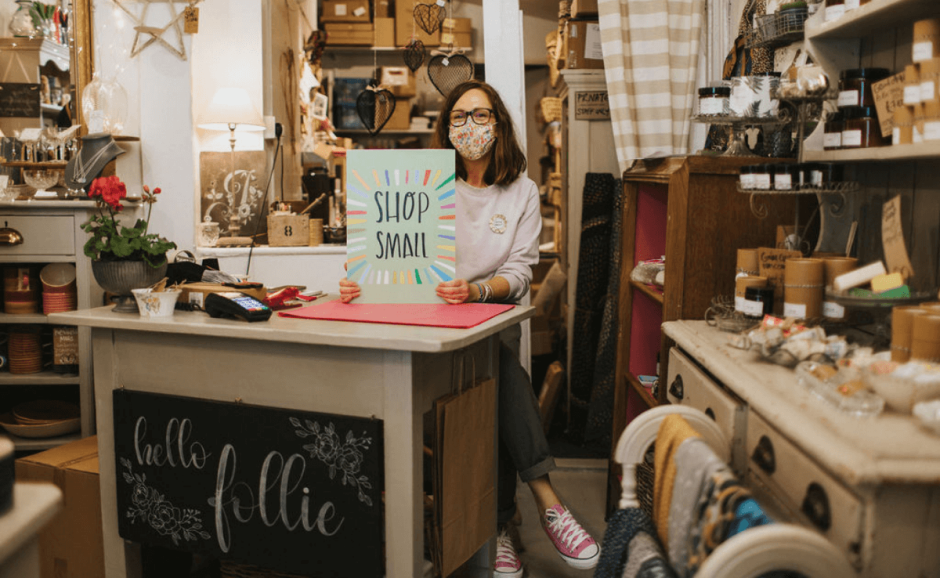 Cozy shop with owner holding a "Shop Small" sign.