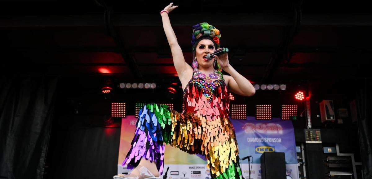 Drag artist dressed in rainbow sequins jumpsuit singing onstage at Southampton Pride