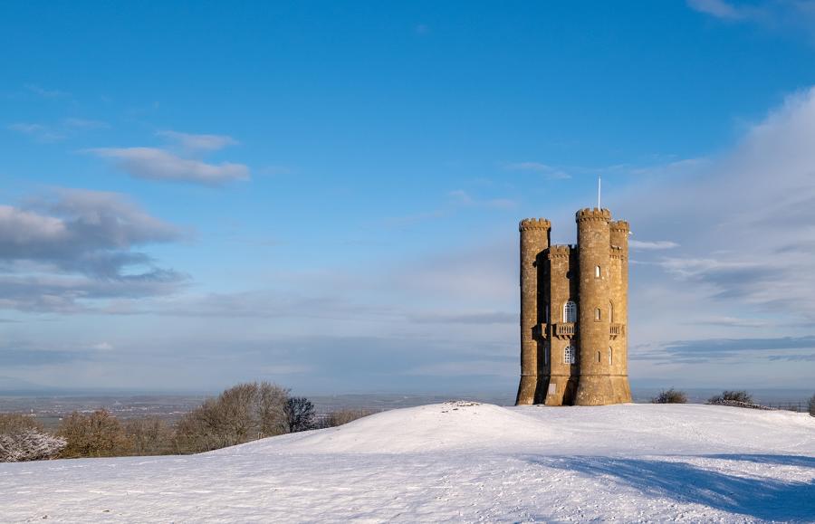 Historic Broadway Tower stands overlooking snow covered countryside on a bright winter's day