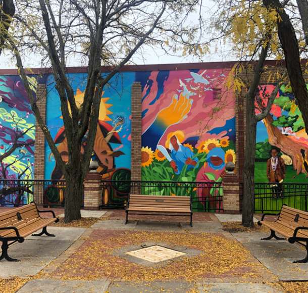 Benches and trees in front of four mural segments in Overland Park