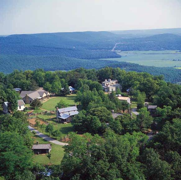 An aerial view of Burritt on the Mountain in Huntsville shows the historic park’s buildings, walking paths, and green spaces surrounded by forested mountain scenery overlooking the Tennessee Valley below.