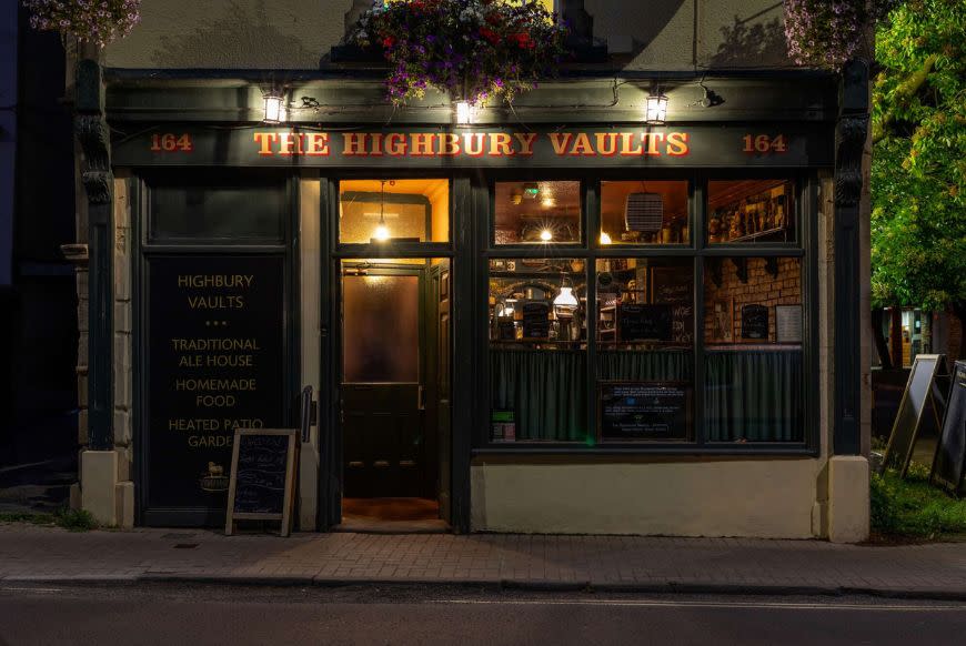 Photo of the outside of the highbury vaults pub, it's dark outside and the front is illuminated by lights