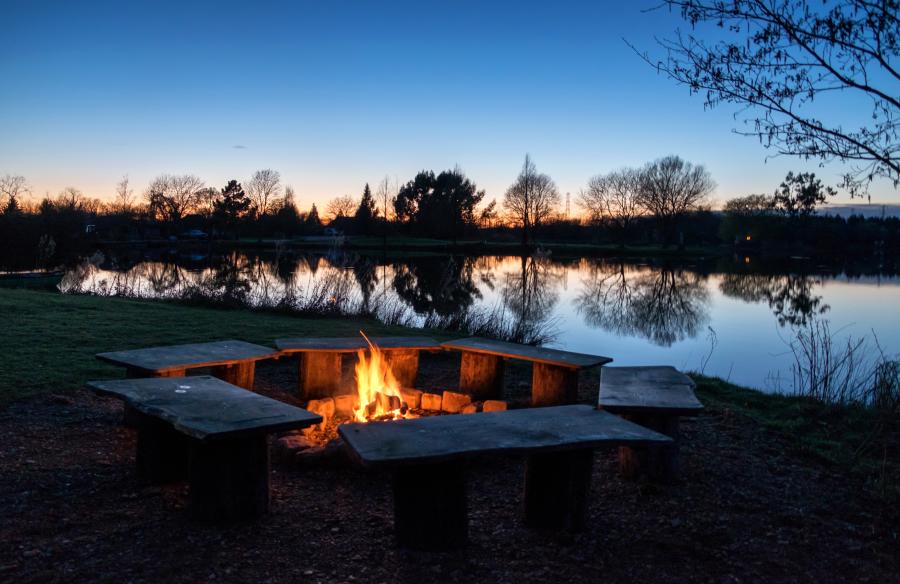 Fire pit lit late at night with the lake in the background and the sun setting at Log House Holidays