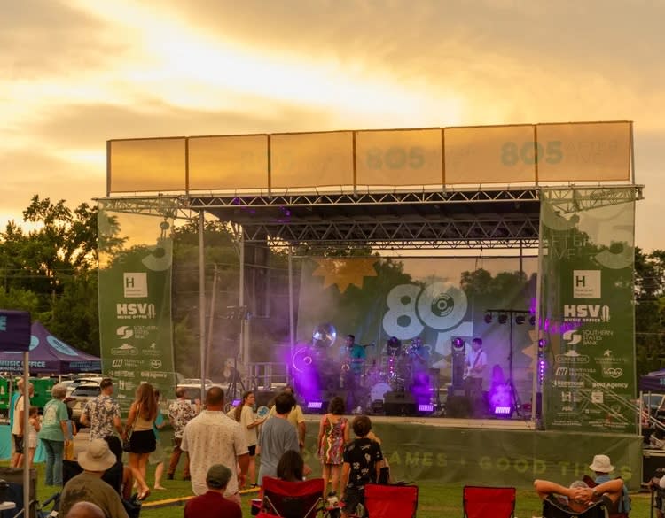 Guests gather on the lawn at Campus No. 805 for 805 After Five, watching a live band perform on the outdoor stage as the sun sets. Attendees relax in lawn chairs and stand near the stage while enjoying an evening of live music and community.