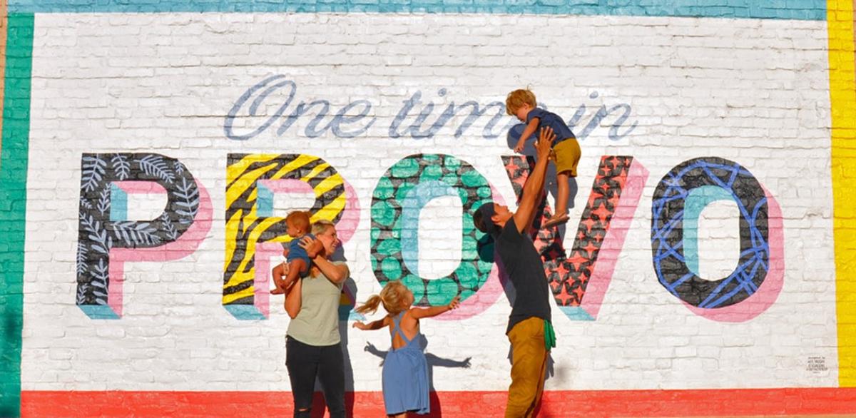 Bucket List Family consisting of 2 adults and 3 kids pose in front of Provo mural that reads "One Time in Provo"