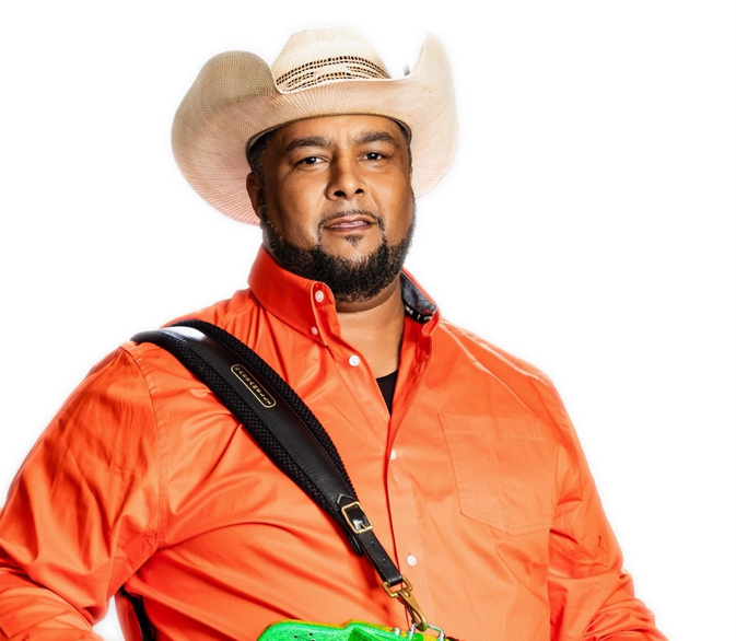 Singer Keith Frank poses for a photo wearing a white stray cowboy hat, orange shirt.