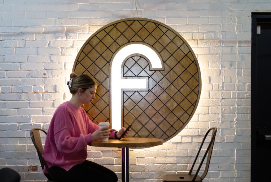 young woman at a table with coffee in hand looking at her phone