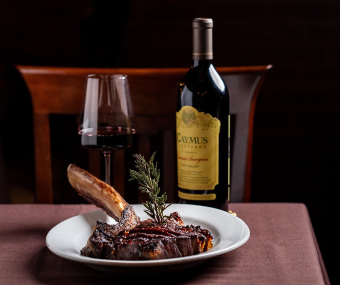 Grilled steak on a plate next to a bottle of wine and a wine glass.