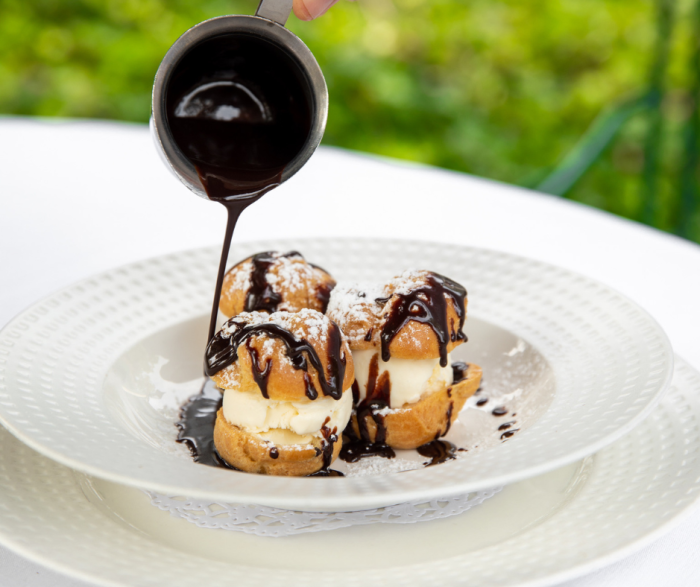 Someone pouring chocolate sauce on top of a cream puff dessert