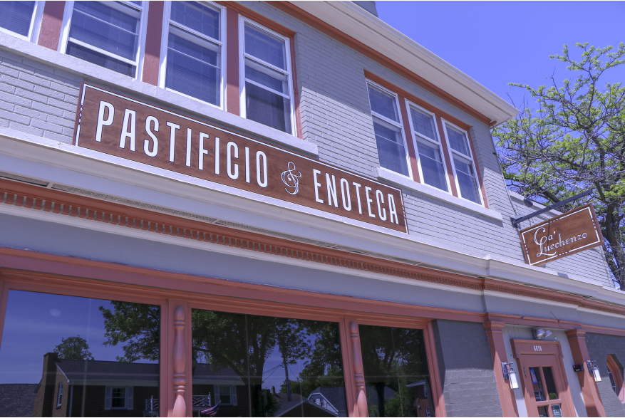 Exterior of Ca’Lucchenzo Pastificio & Enoteca, a light brick neighborhood restaurant with coral colored trim, tall second-floor windows and a large Pastificio & Enoteca sign above the storefront entrance.