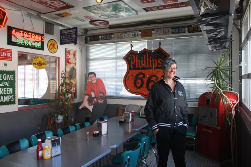 Summer Willis stands in the private dining area of 66 Diner, with a cardboard cut-out of Elvis Presley, a large Phillips 66 shield sign, and various retro Americana decorations.