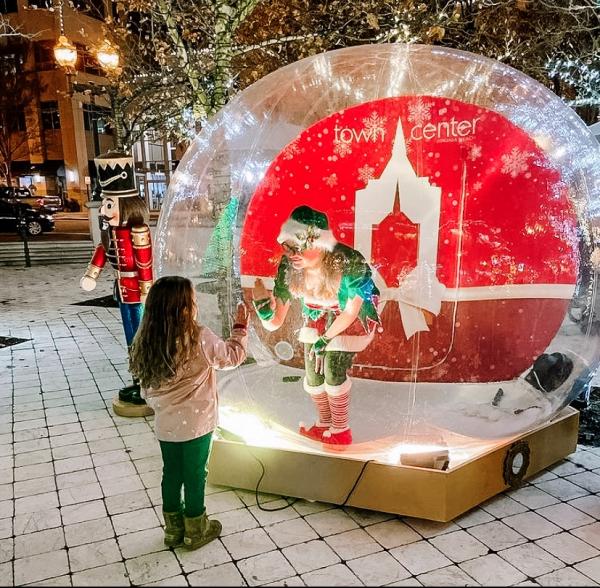 Elf inside a Snow Globe touching hands through the glass with a little girl in Town Center