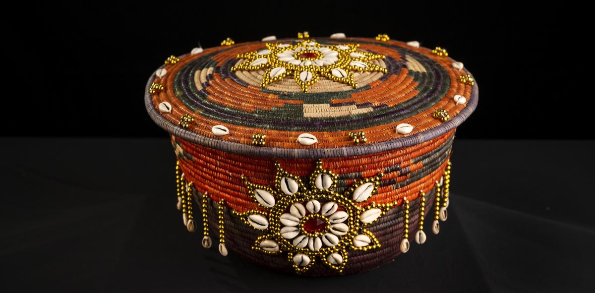 A Sudanese Mandola which is a woven vessel used to hold food, it has shells and beads on it as decoration.