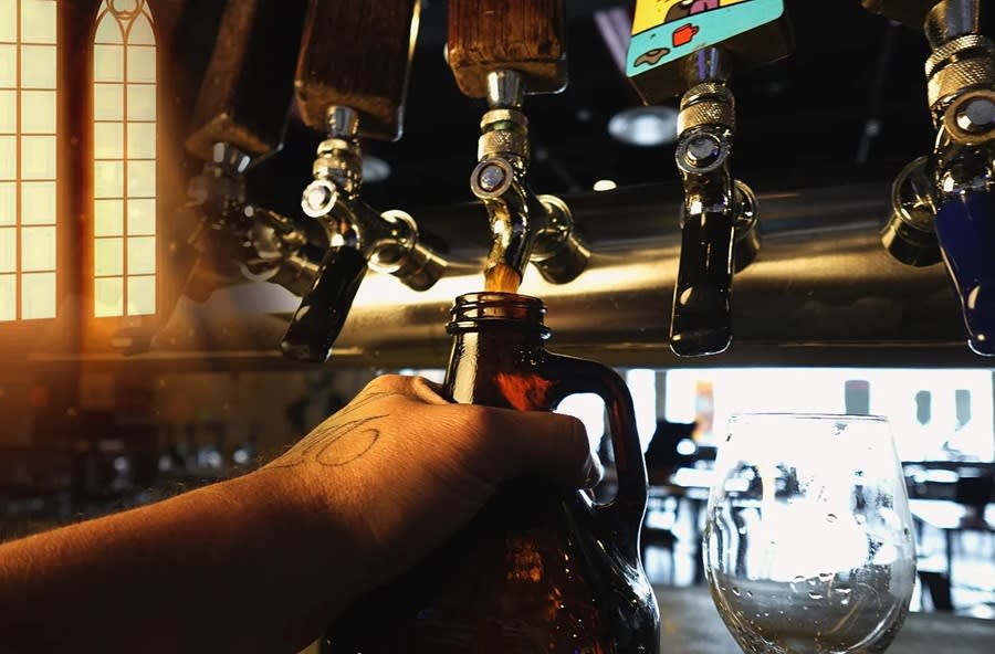 the hand of a bartender filling a growler of beer from a tap