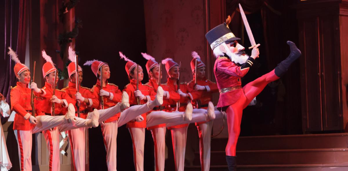 Toy soldiers played by children are lined up on stage behind a man in a nutcracker costume.