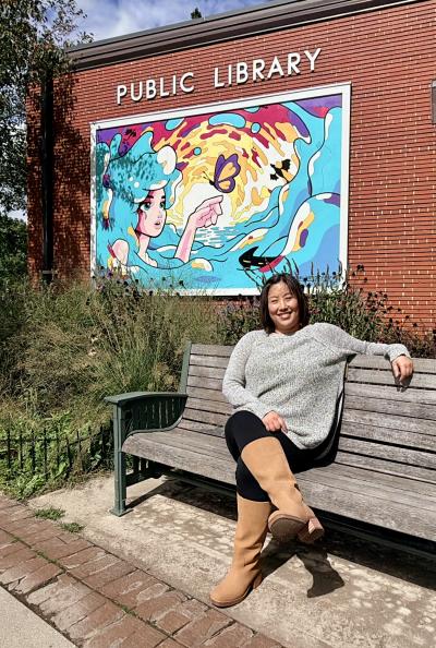 Picture of Library Director Emily Kornak under a mural on the lakeside of the library building.