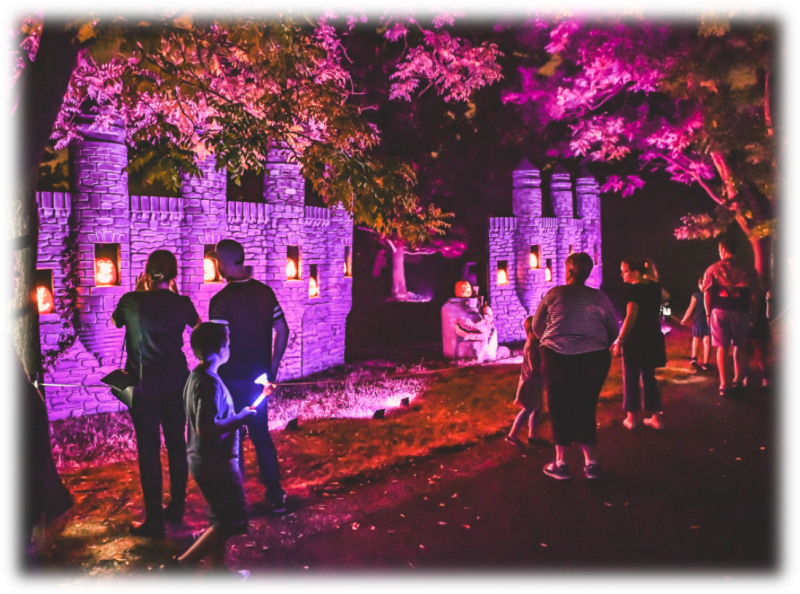 Families at Lincoln Hill Farms at night, looking at jack-o'-lanterns on a castle wall