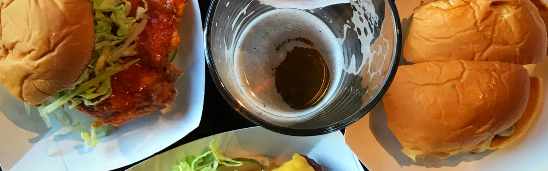 Bird's-eye view of burgers, sandwiches and fried chicken from Preston's Burgers surrounding pint of beer
