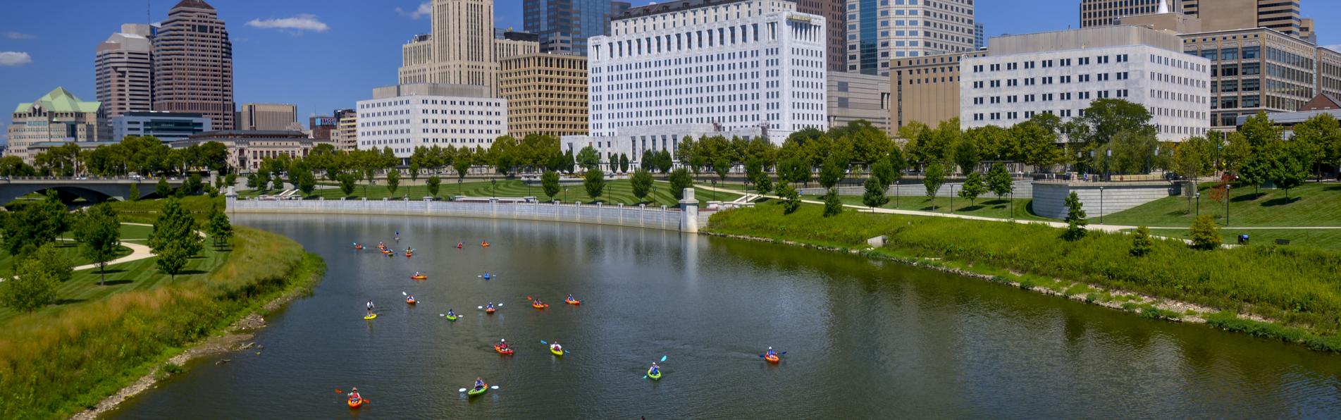 Kayakers float on the Scioto River with the Columbus skyline in the background