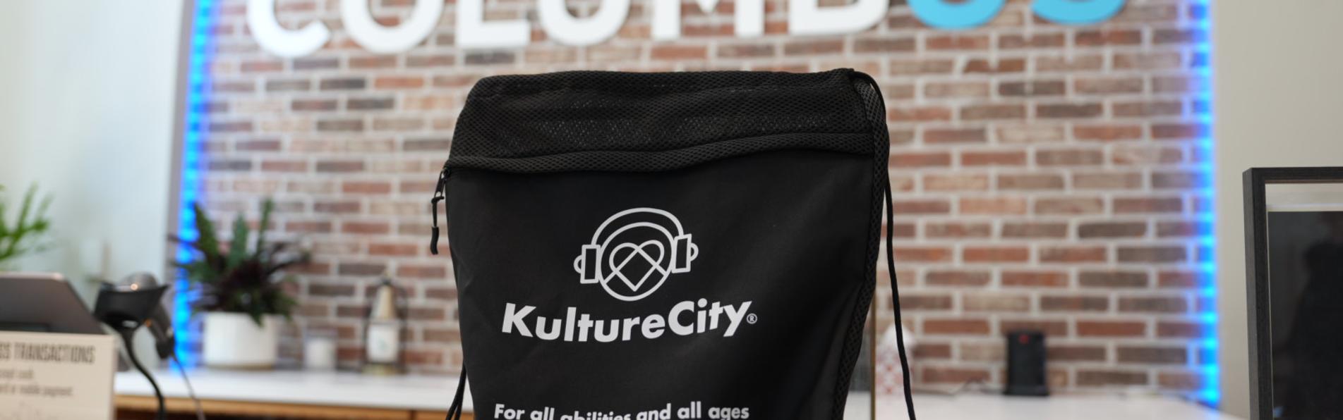 A black KultureCity drawstring sensory bag sits upright on a white counter with a Columbus sign in the background at the Columbus Welcome Center