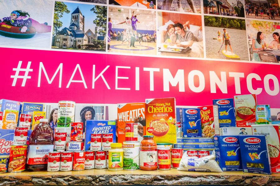 Canned goods and non-perishables are placed on a table in front of a #MakeItMontco sign