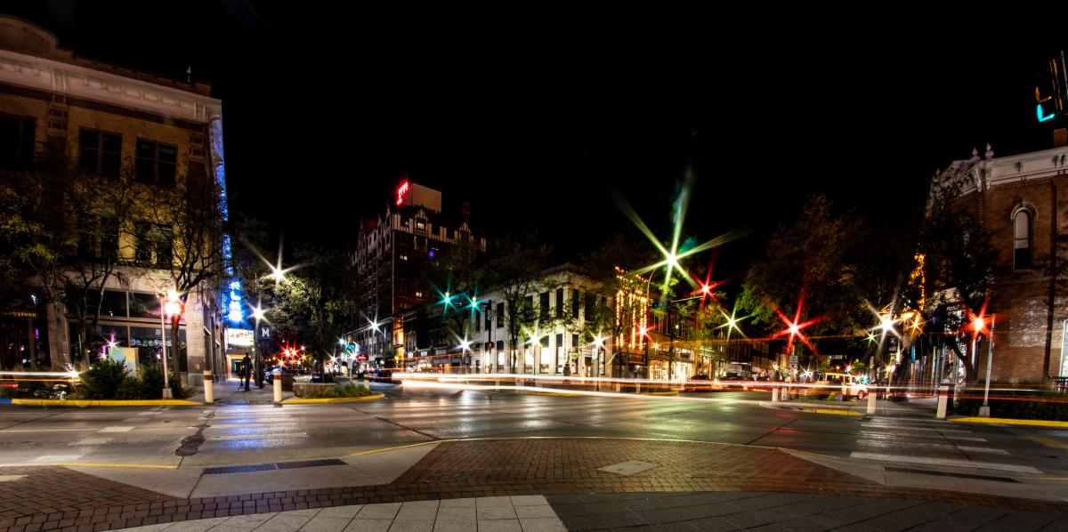 Long-exposure nighttime view of downtown Rapid City, with historic buildings, glowing streetlights, and colorful light trails from passing traffic.