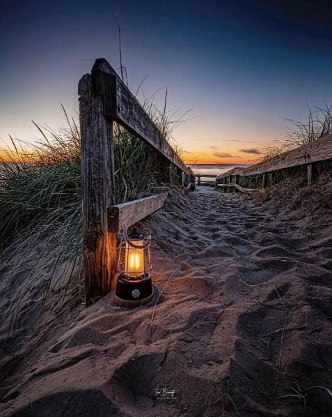 glowing lantern sits in beach sand along wooden fencing leading to lake michigan at sunset