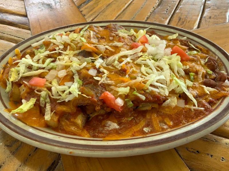 A plate of chile rellenos covered in chile, cheese, lettuce and tomato.