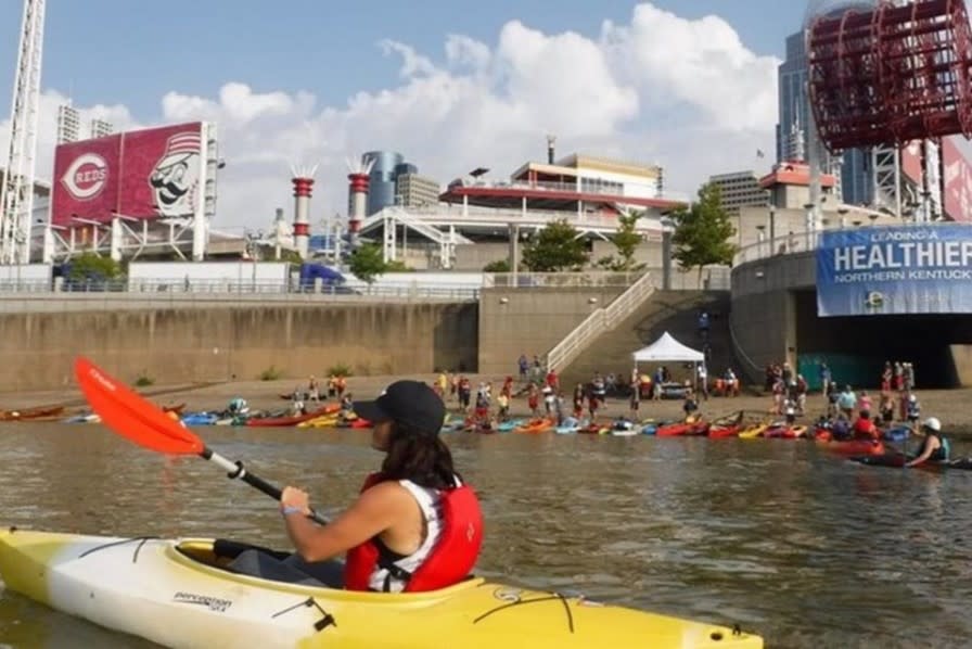 Woman in a kayak with other kayaks and canoes in the background on the Ohio river with the Great American ballpark in the background