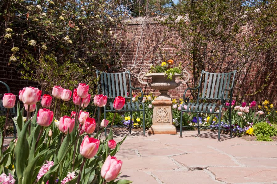 outdoor chairs in flower garden area with brick wall behind