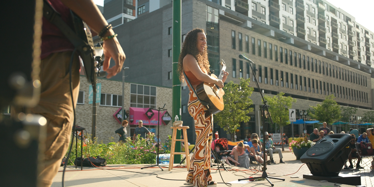 Women with guitar playing and singing on stage in the summer in downtown Lansing