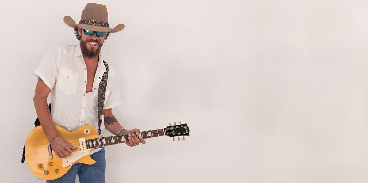 County singer Chris Janson poses for a photo wearing a cowboy hat, jeans and holding a guitar.