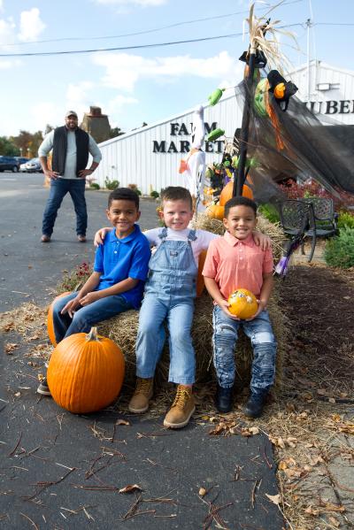 Three boys posing on a hay bale with pumpkins at Joe Huber's 