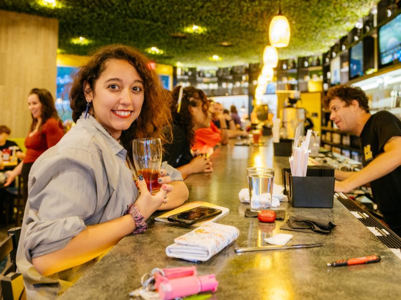 A woman smiles as she drinks a beer at the bar at Brekki Brekki.