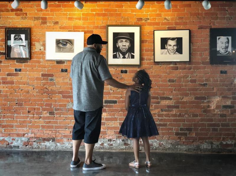 Father and daughter admiring father's artwork hanging on brick wall